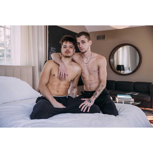 Two topless males wearing jeans on bed caressing